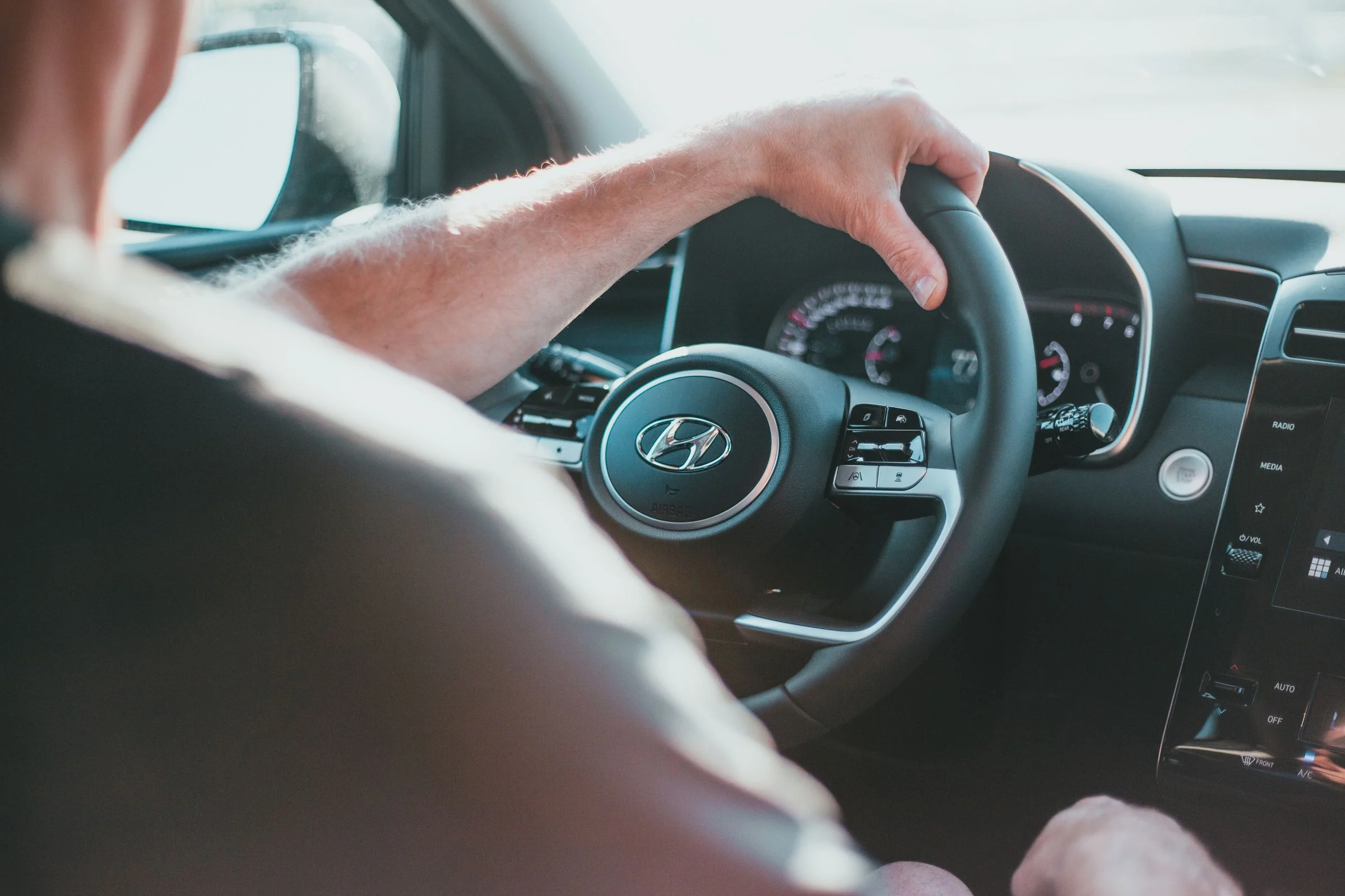 Mãos de um motorista adulto no volante, vistas de dentro do carro, com o painel ao fundo