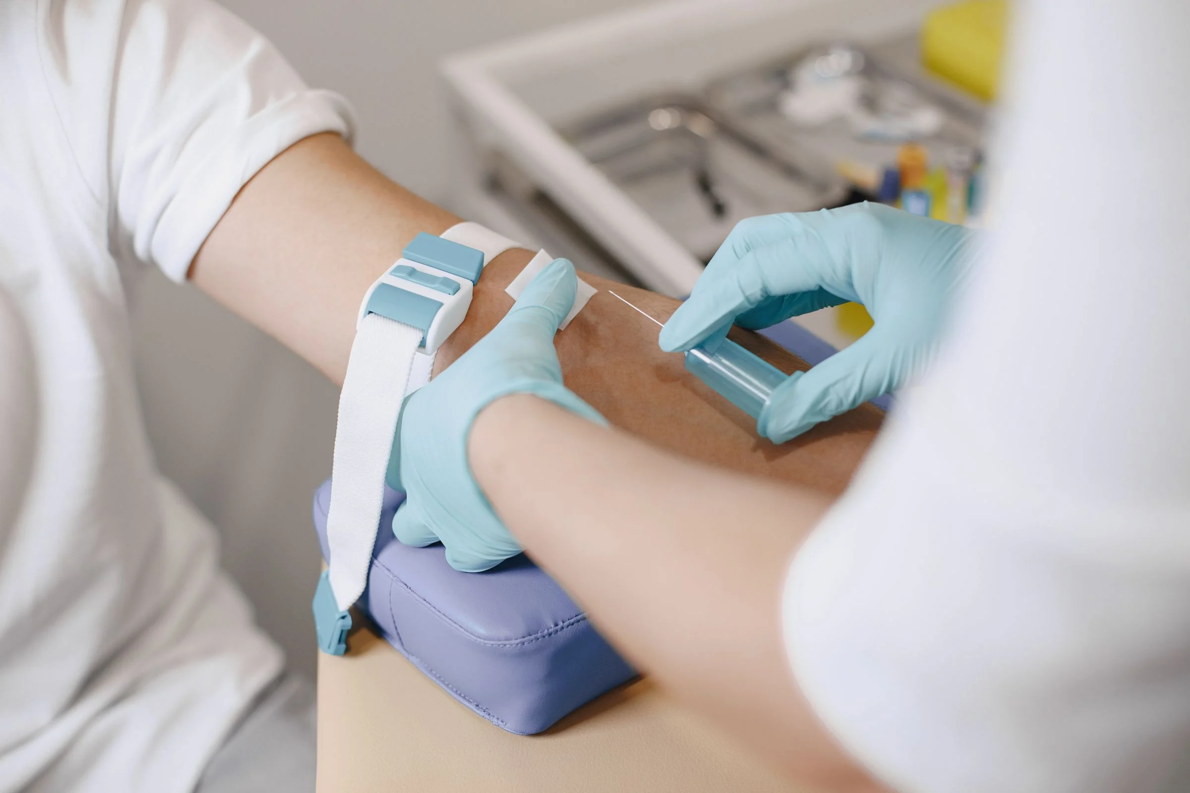 Coleta de sangue no braço de um paciente, feita por profissional de luvas