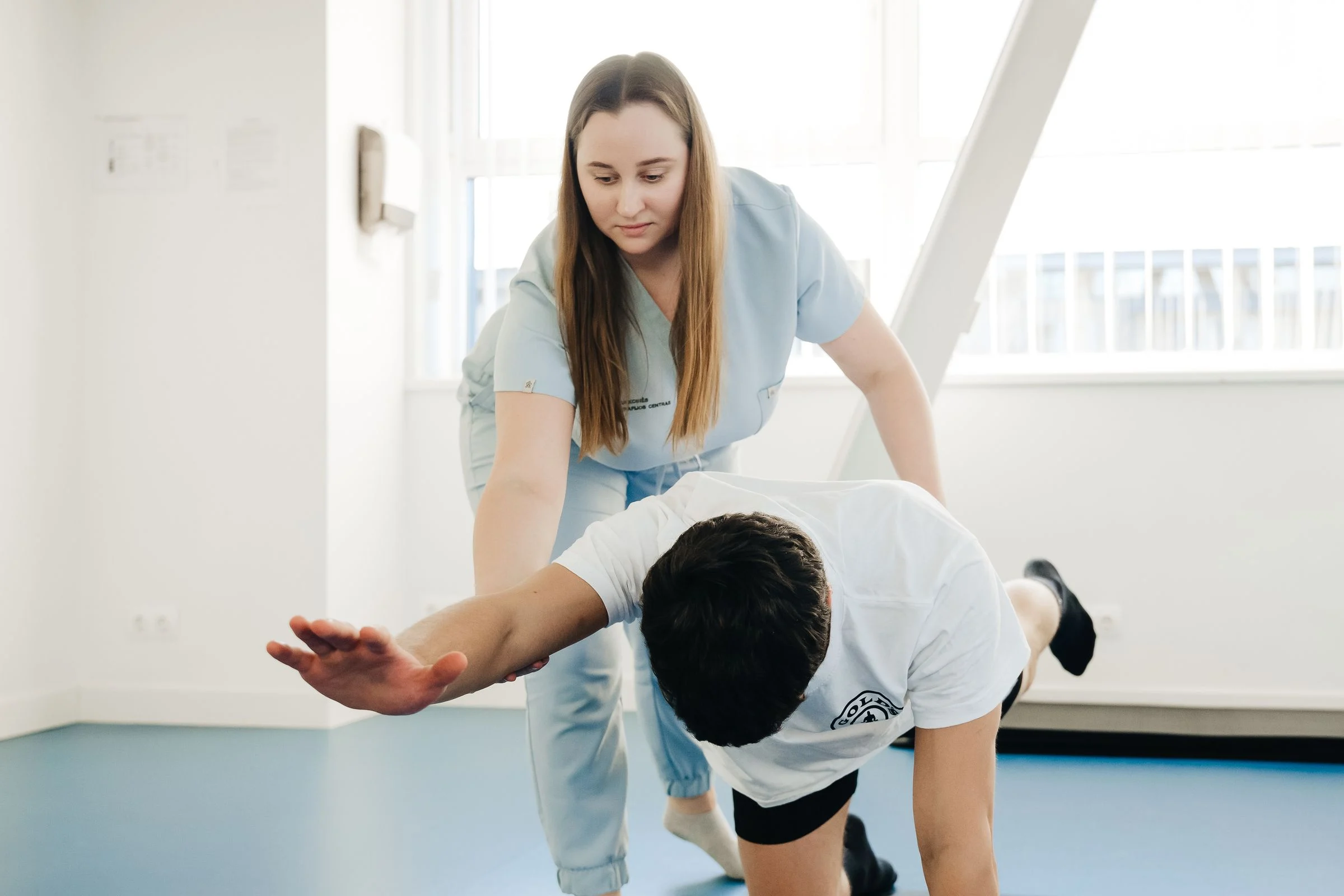 Fisioterapeuta orientando um paciente durante um exercício em pé, numa sala de reabilitação
