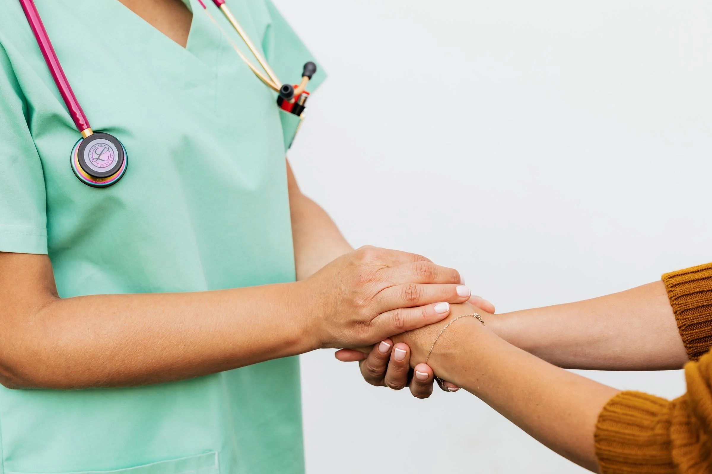 Profissional de saúde segurando com as duas mãos a mão de um paciente
